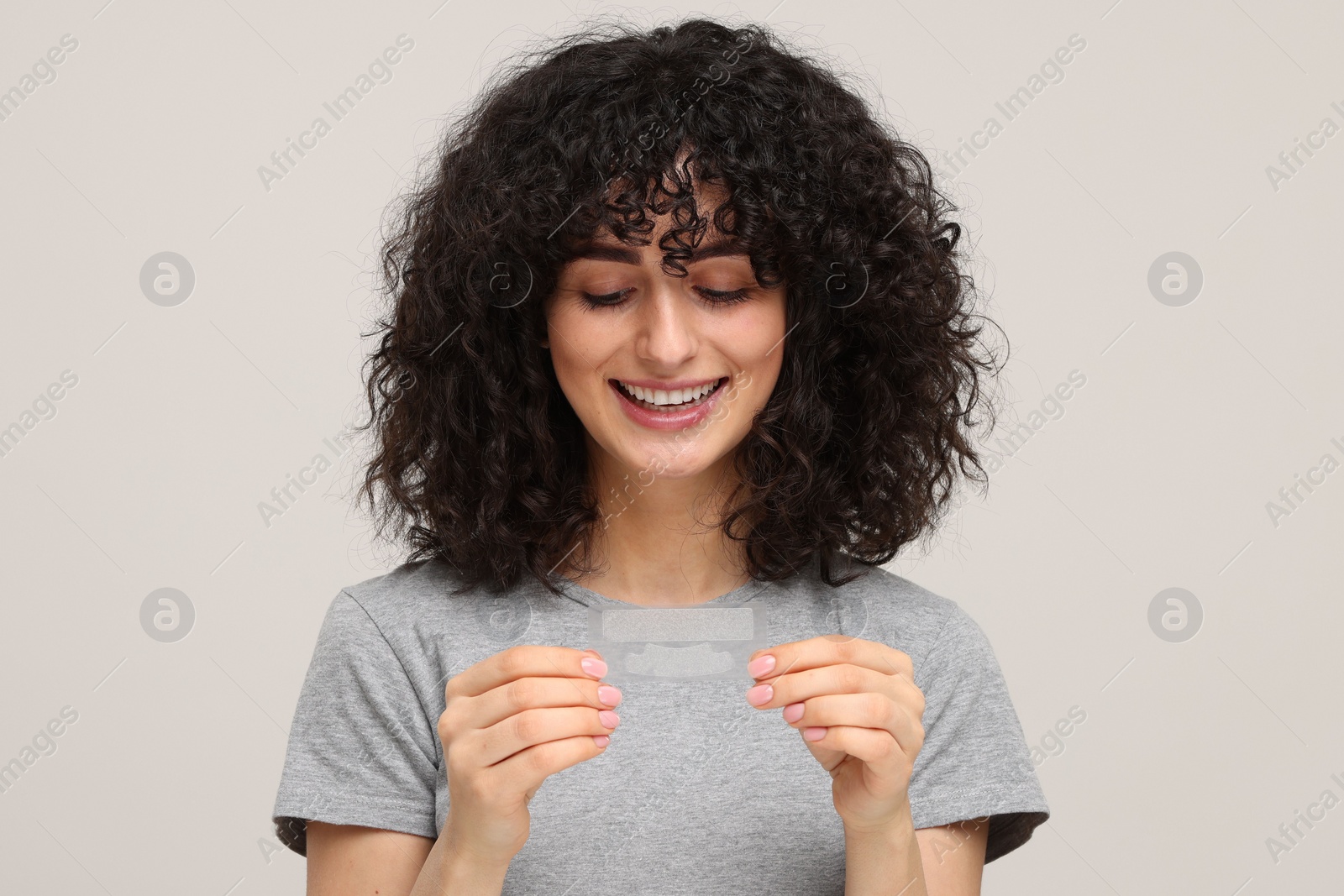 Photo of Young woman holding teeth whitening strips on light grey background