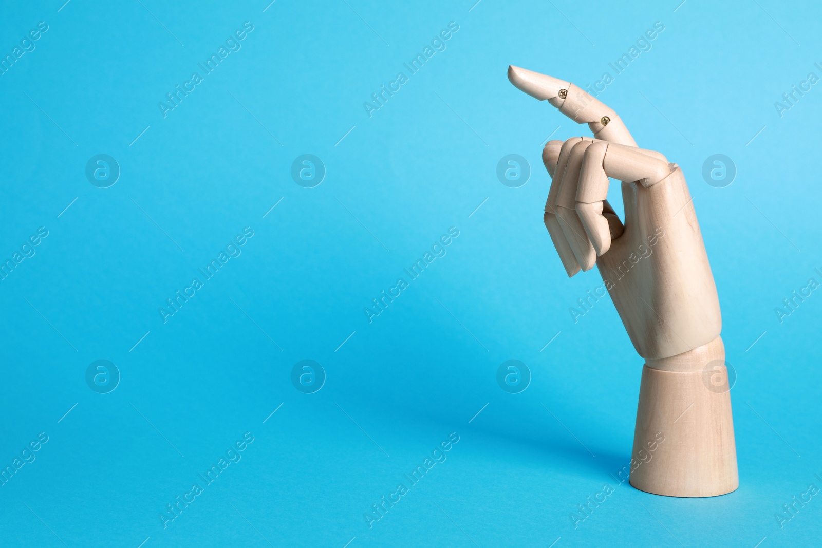 Photo of Wooden mannequin hand on light blue background. Space for text