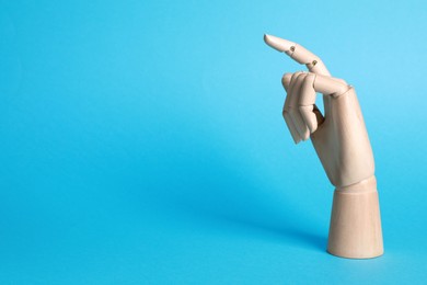 Photo of Wooden mannequin hand on light blue background. Space for text