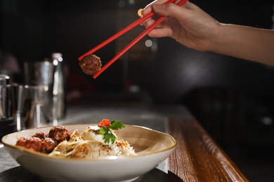 Photo of Woman eating rice and meatballs with chopsticks at table, closeup