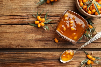 Delicious sea buckthorn jam and fresh berries on wooden table, flat lay. Space for text