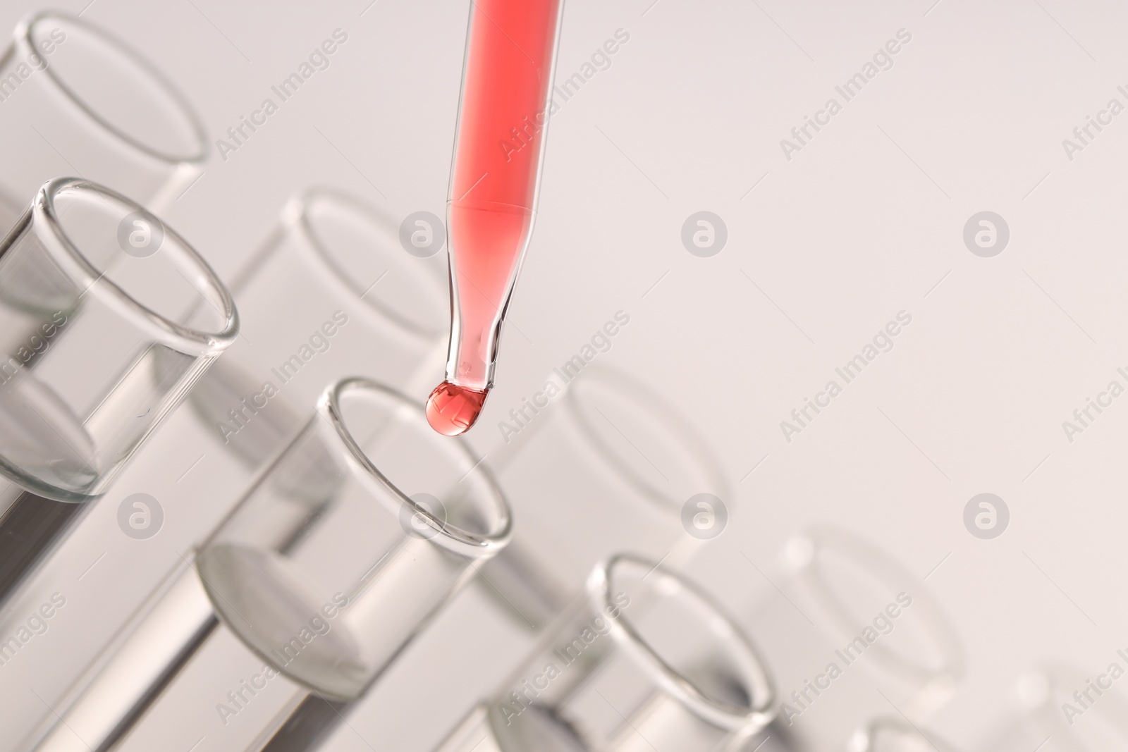 Photo of Dripping liquid from pipette into test tube on light background, closeup. Space for text