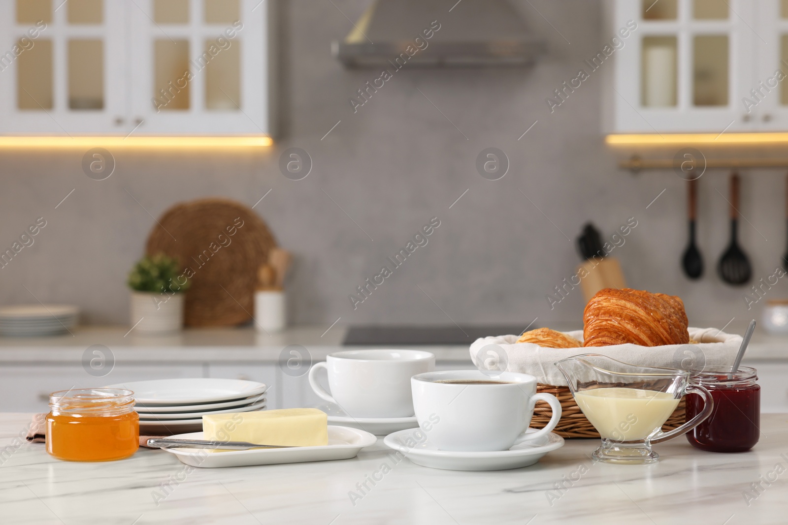 Photo of Breakfast served in kitchen. Fresh croissants, coffee, butter, jam, honey and sweetened condensed milk on white table