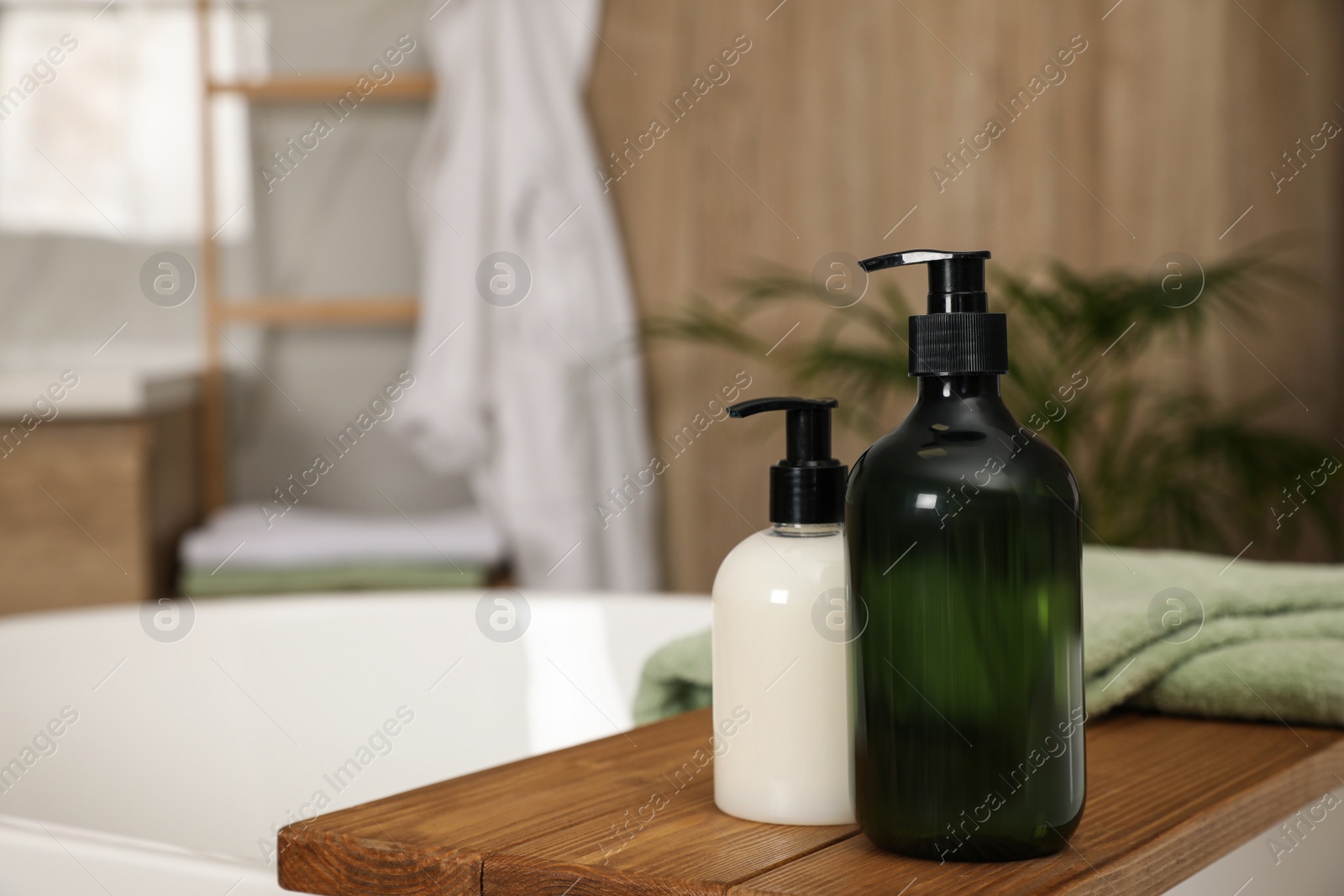 Photo of Wooden bath tray with bottles of shower gels and towel on tub indoors, space for text