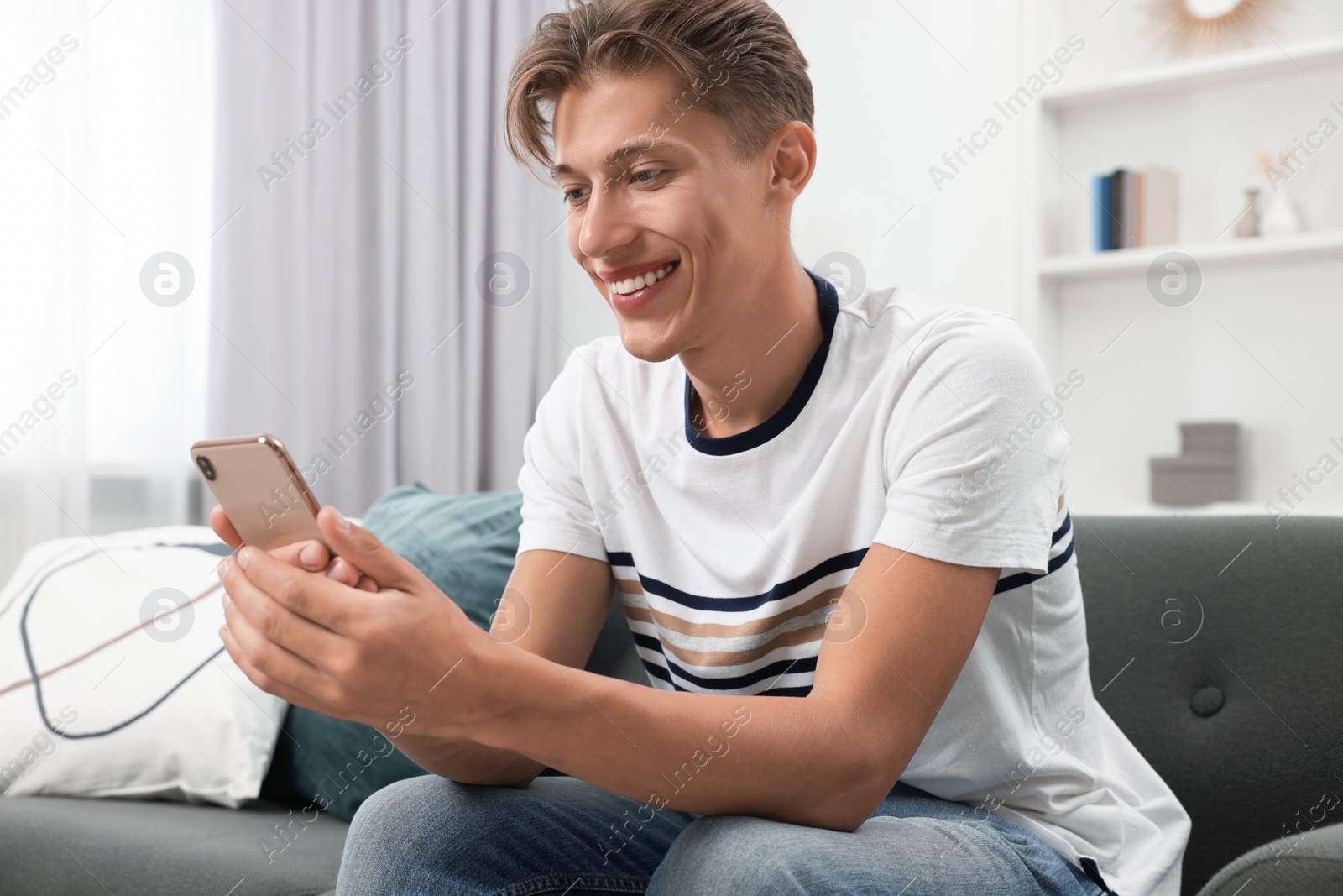 Photo of Happy young man having video chat via smartphone on sofa indoors