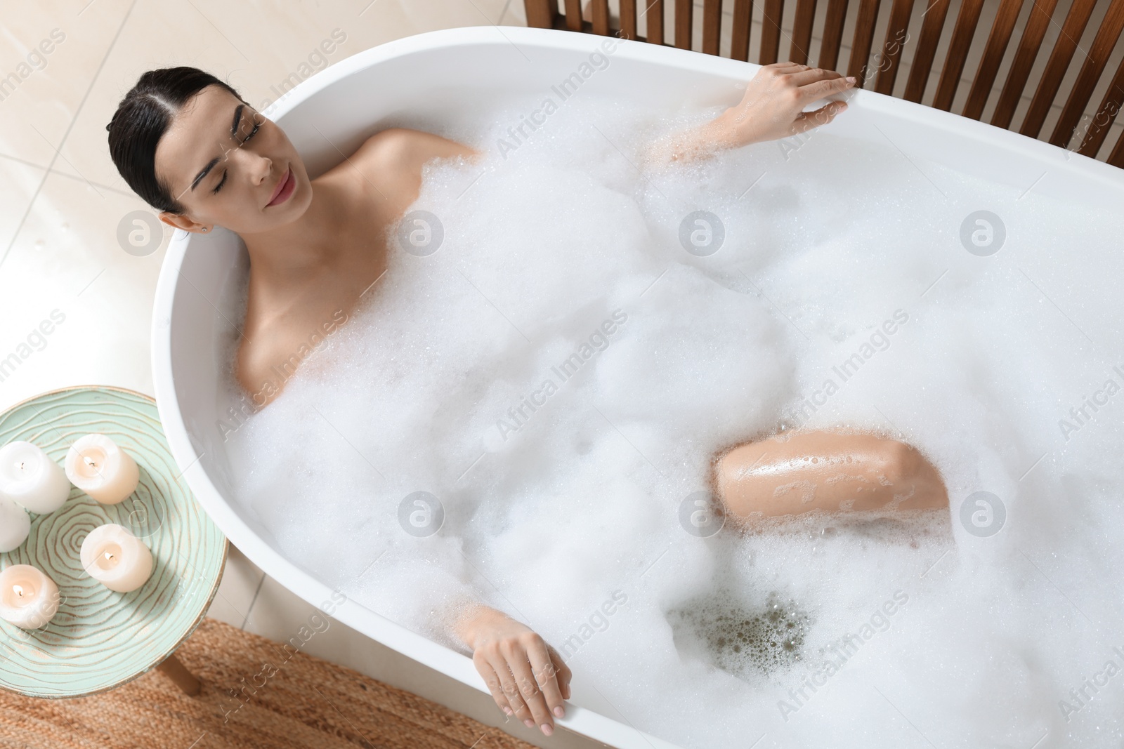 Photo of Beautiful young woman taking bubble bath at home, above view