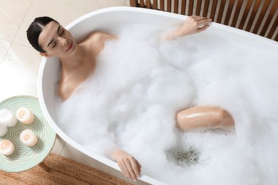 Photo of Beautiful young woman taking bubble bath at home, above view