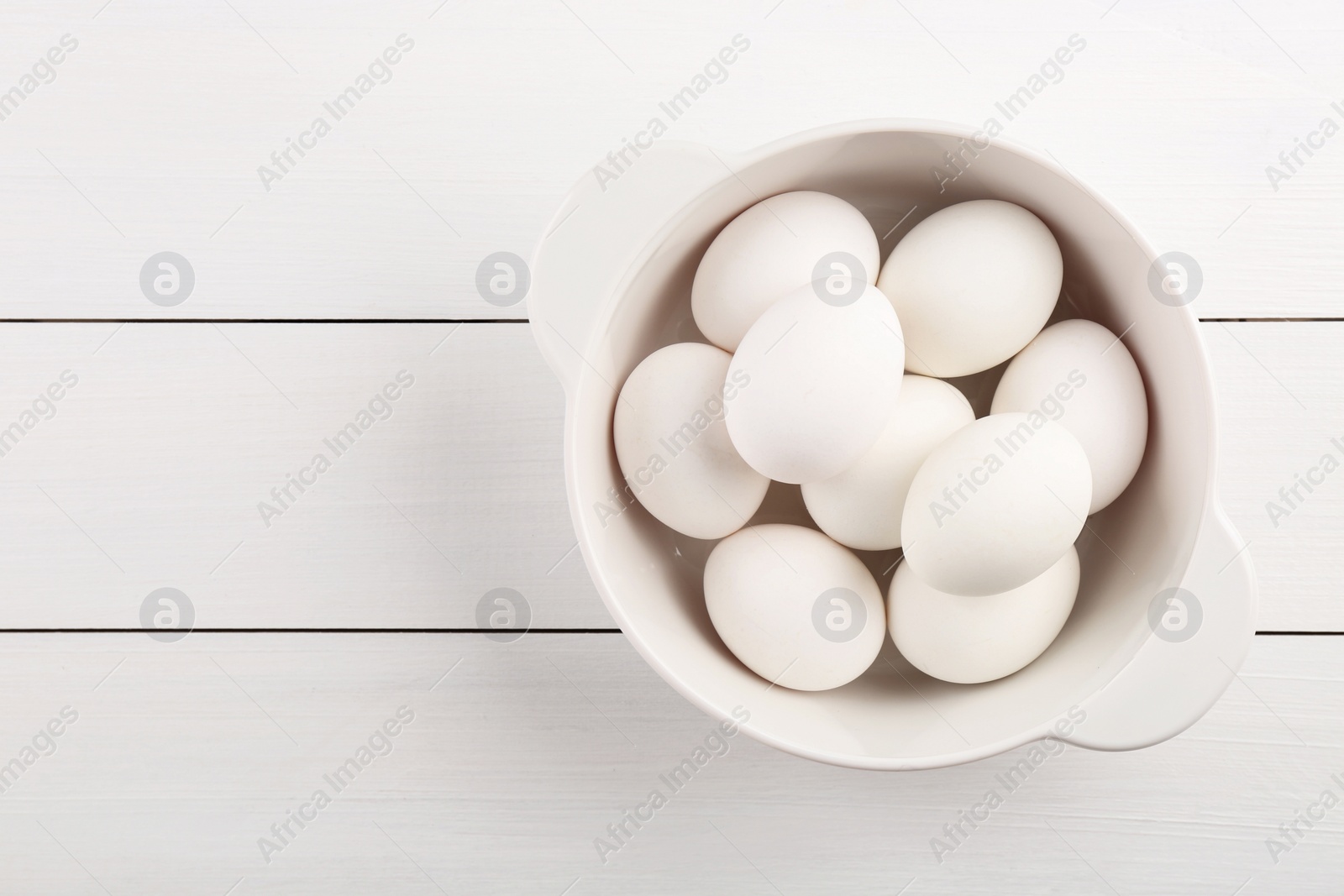 Photo of Boiled eggs in saucepan on white wooden table, top view. Space for text