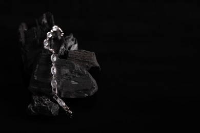 Luxury jewelry. Stylish presentation of elegant bracelet on coal against black background, space for text