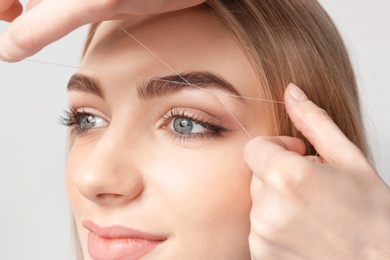 Photo of Young woman having professional eyebrow correction procedure in beauty salon