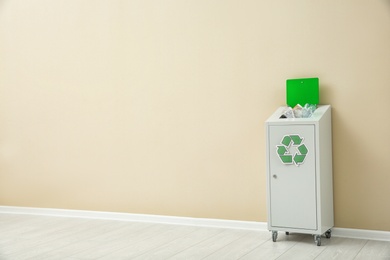 Trash bin with recycling symbol near color wall indoors. Space for text