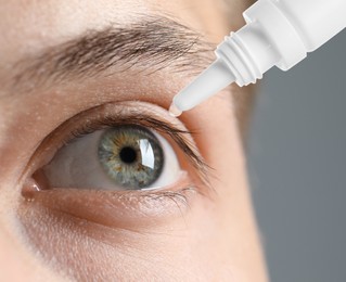 Man applying eye drops on grey background, closeup