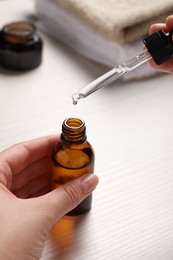 Woman with bottle of cosmetic serum and pipette at white table, closeup