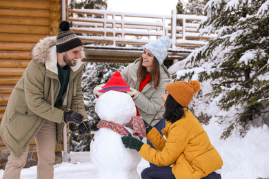 Photo of Happy friends making snowman outdoors. Winter vacation