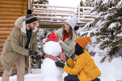 Happy friends making snowman outdoors. Winter vacation