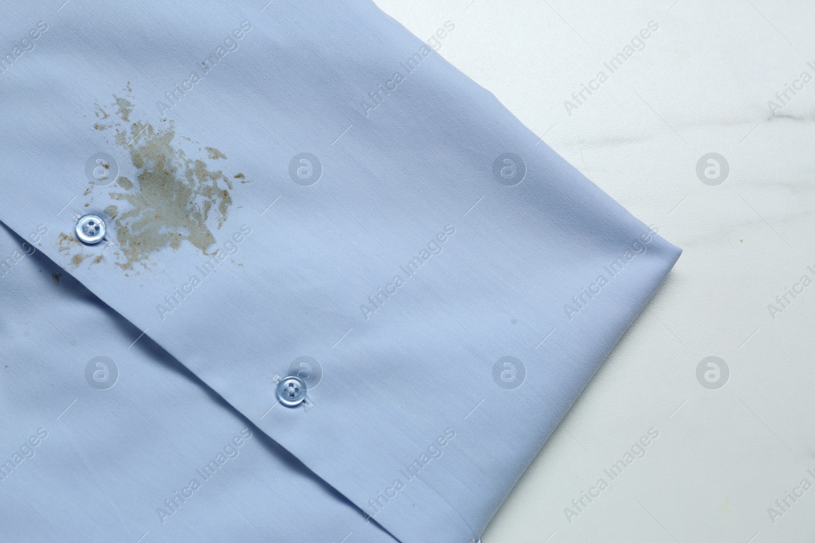 Photo of Light blue shirt with stain on white marble table, top view