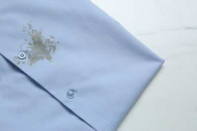 Light blue shirt with stain on white marble table, top view