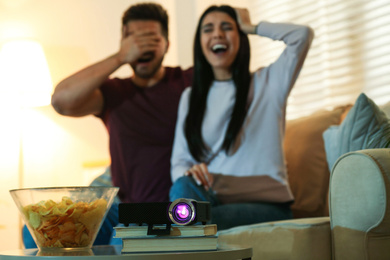 Photo of Young couple watching movie at home, focus on video projector