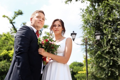 Photo of Happy newlyweds with beautiful bridal bouquet outdoors