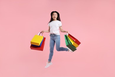 Photo of Happy woman with shopping bags jumping on pink background