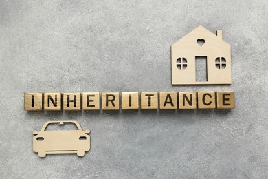 Word Inheritance made with wooden cubes, house and car models on grey background, flat lay