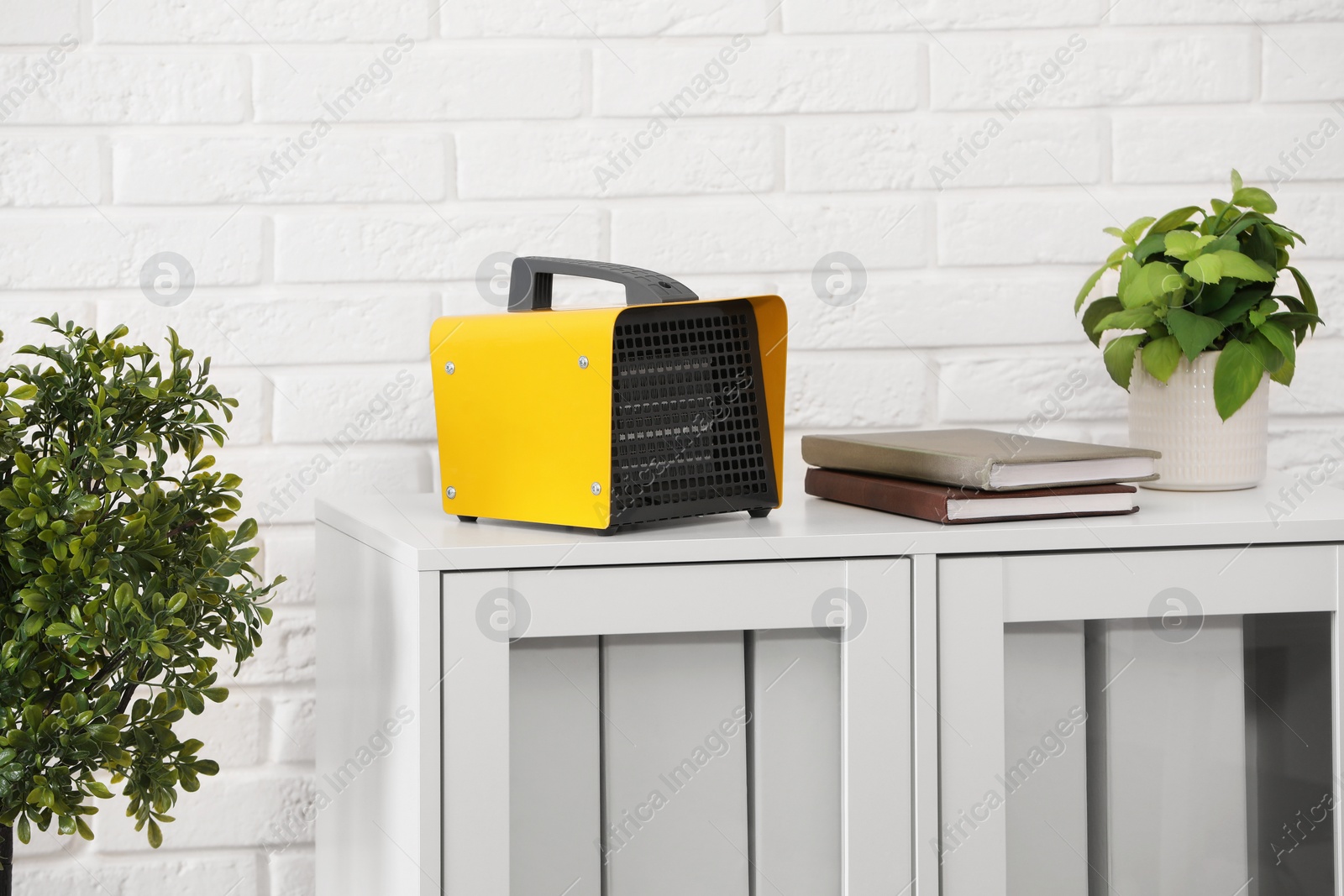 Photo of Modern electric fan heater near notebooks and houseplant on white table indoors