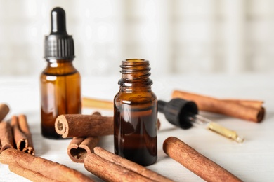 Photo of Bottles of essential oils and cinnamon sticks on white wooden table