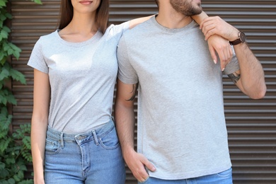 Photo of Young couple wearing gray t-shirts near wall on street.