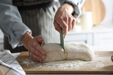Photo of Woman cutting dough at white wooden table in kitchen, closeup
