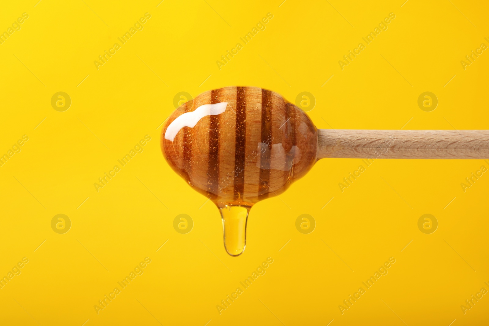 Photo of Pouring honey from dipper against yellow background, closeup