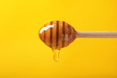 Pouring honey from dipper against yellow background, closeup