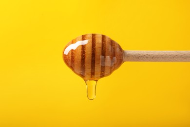 Photo of Pouring honey from dipper against yellow background, closeup