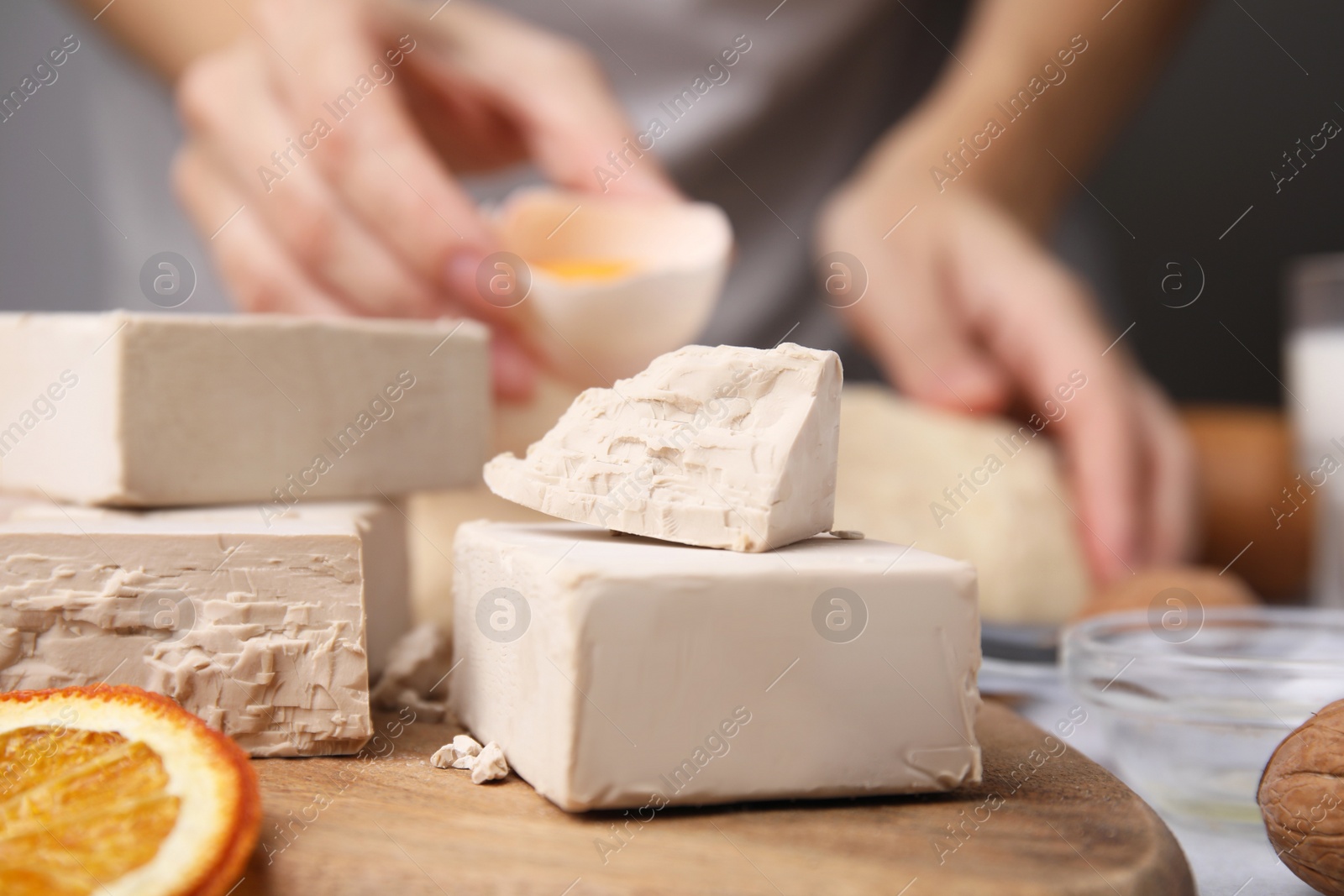 Photo of Woman kneading dough at table, focus on blocks of compressed yeast