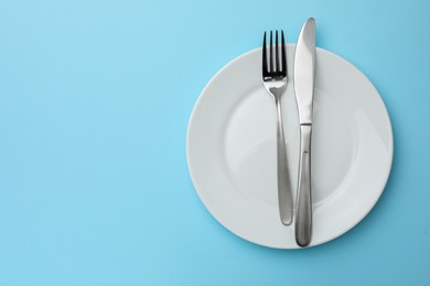 Photo of Clean plate, fork and knife on light blue background, top view. Space for text