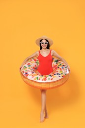 Happy young woman with beautiful suntan, hat, sunglasses and inflatable ring against orange background