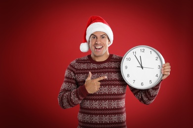 Photo of Man in Santa hat with clock on red background. New Year countdown