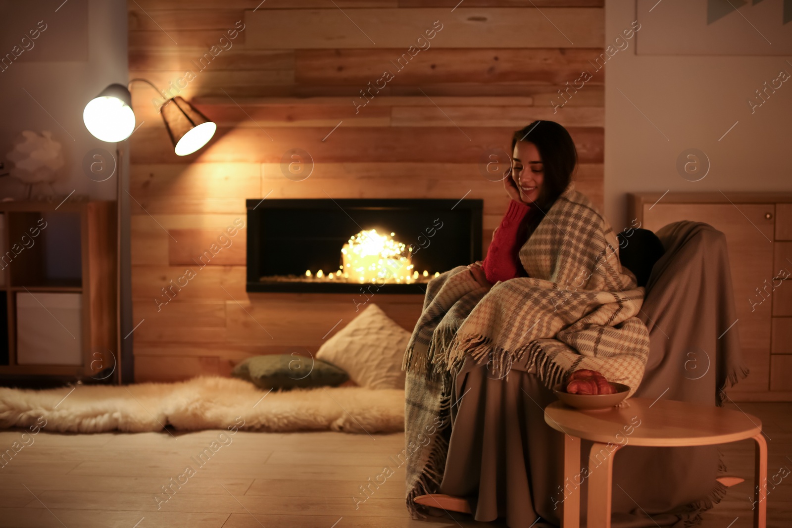 Photo of Young woman resting near decorative fireplace at home. Winter season