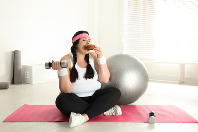 Lazy overweight woman eating bun at gym