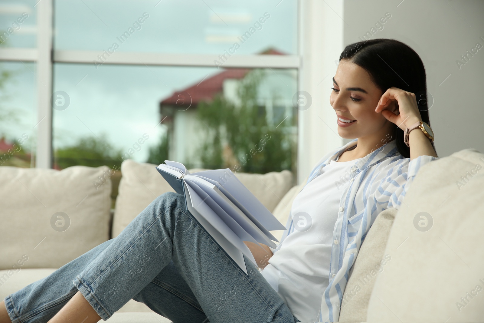 Photo of Young woman reading book on sofa at home