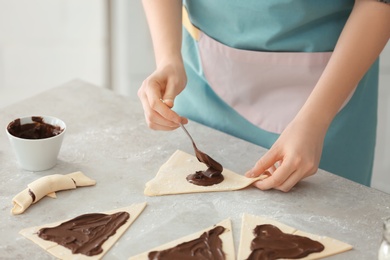 Photo of Woman preparing tasty croissants with chocolate paste on table, closeup