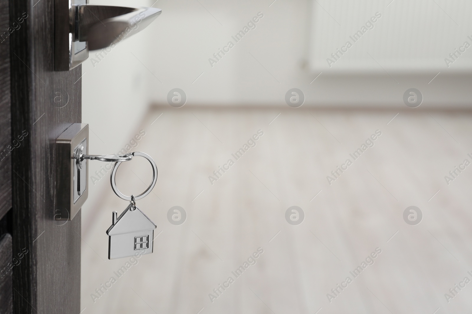 Photo of Mortgage and real estate. Open door with key and house shaped keychain against blurred background, space for text