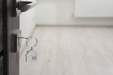 Photo of Mortgage and real estate. Open door with key and house shaped keychain against blurred background, space for text