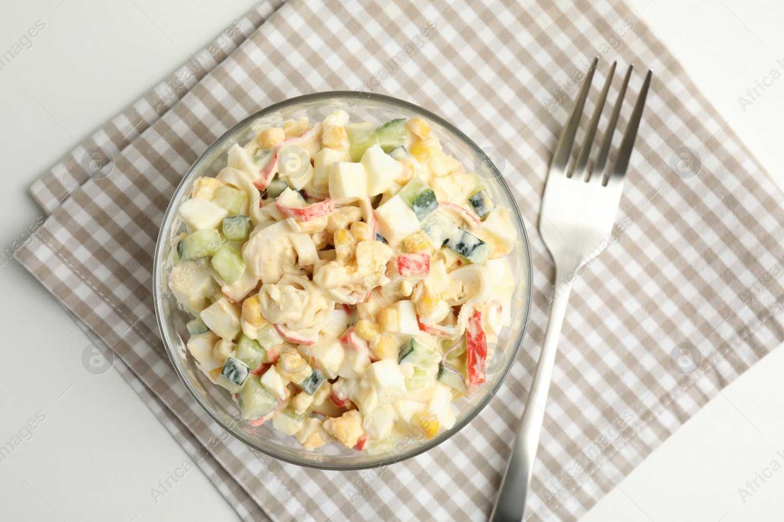 Photo of Delicious salad with fresh crab sticks in glass bowl on white table, top view