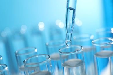 Dripping liquid from pipette into test tube on light blue background, closeup