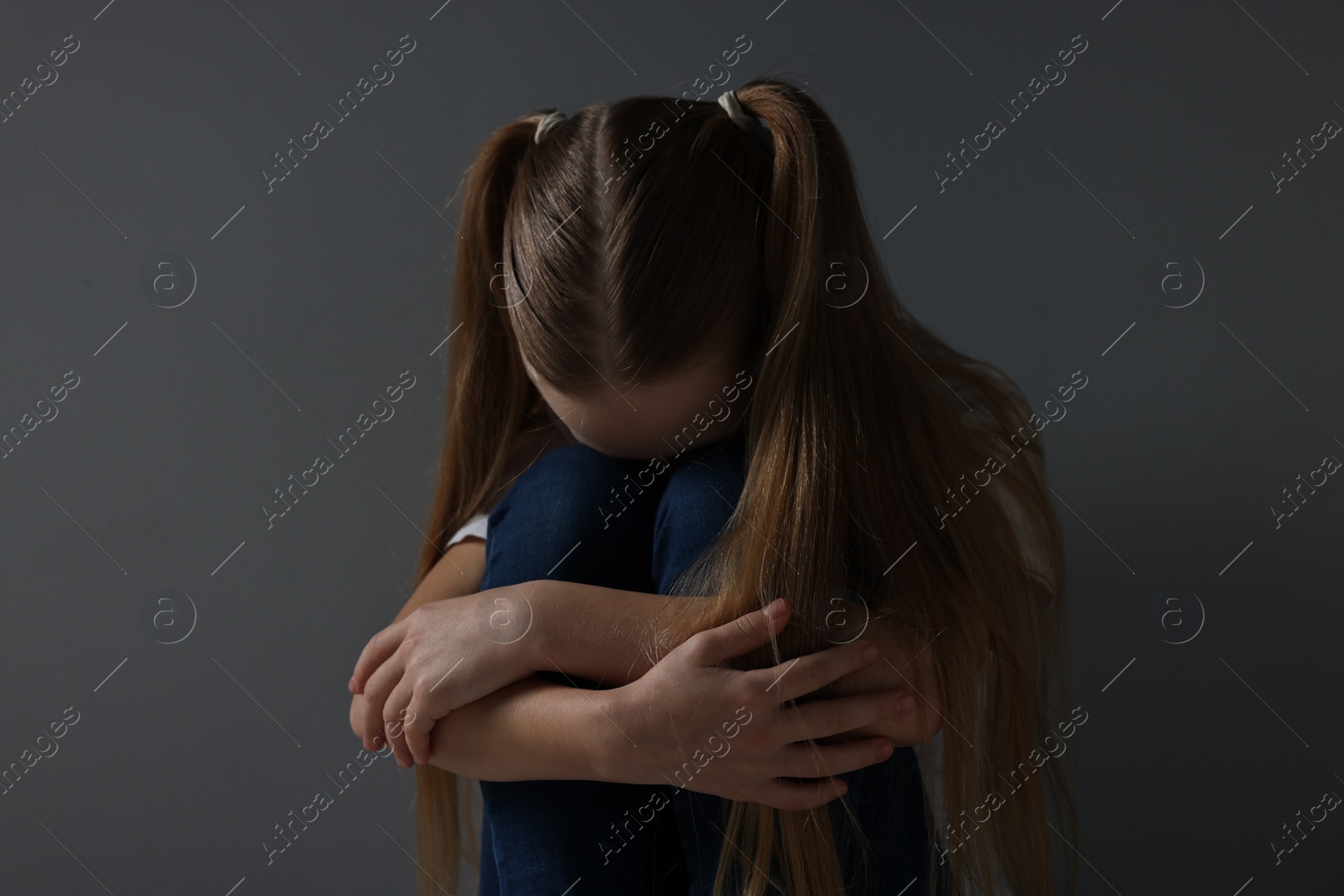 Photo of Sad girl sitting near dark grey background