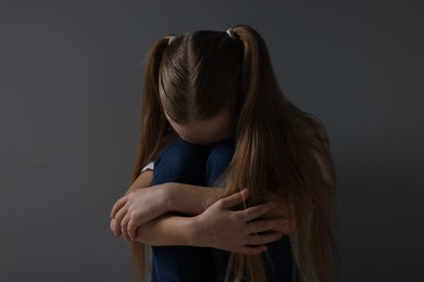 Photo of Sad girl sitting near dark grey background