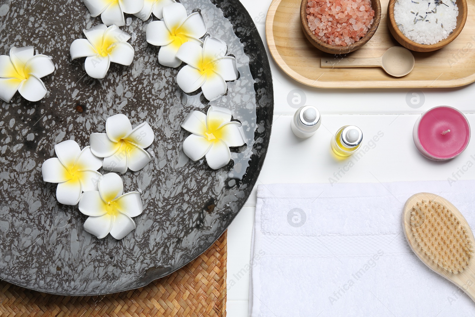 Photo of Bowl of water with flowers and different spa supplies on white wooden table, flat lay