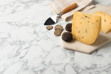 Photo of Delicious cheese and fresh black truffles on white marble table. Space for text