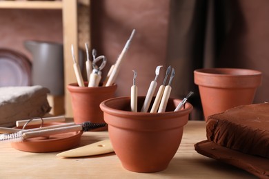 Photo of Set of different clay crafting tools on wooden table in workshop