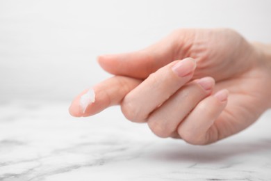 Photo of Woman applying petroleum jelly onto her finger at white table, closeup